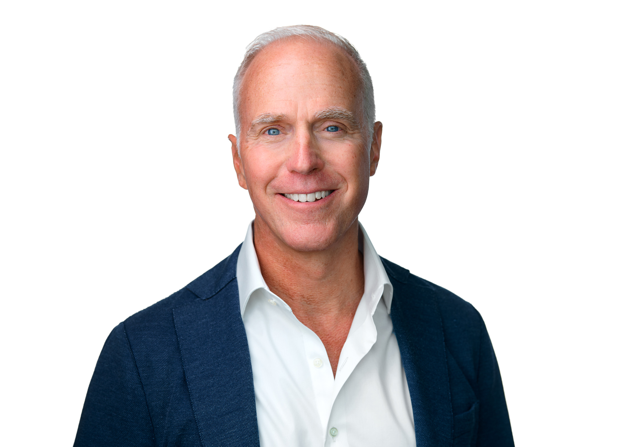 Headshot of a man with short gray hair smiling, wearing a navy blazer and white shirt against a light background